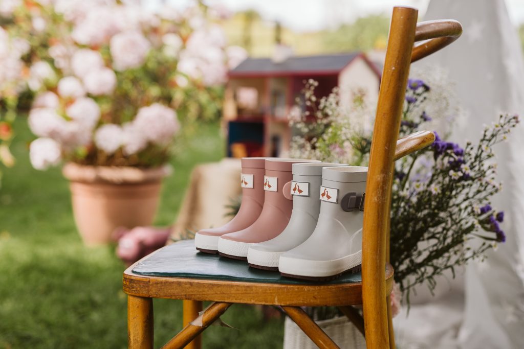 Kids Pink and Grey waterproof wellies on a wooden chair outside next to some flowers. 