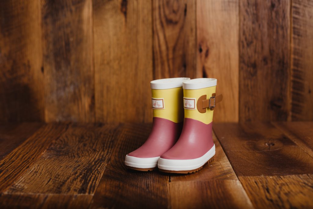  Goose and gander waterproof kids wellies in a rhubarb and custard colour on a brown wooden backdrop.